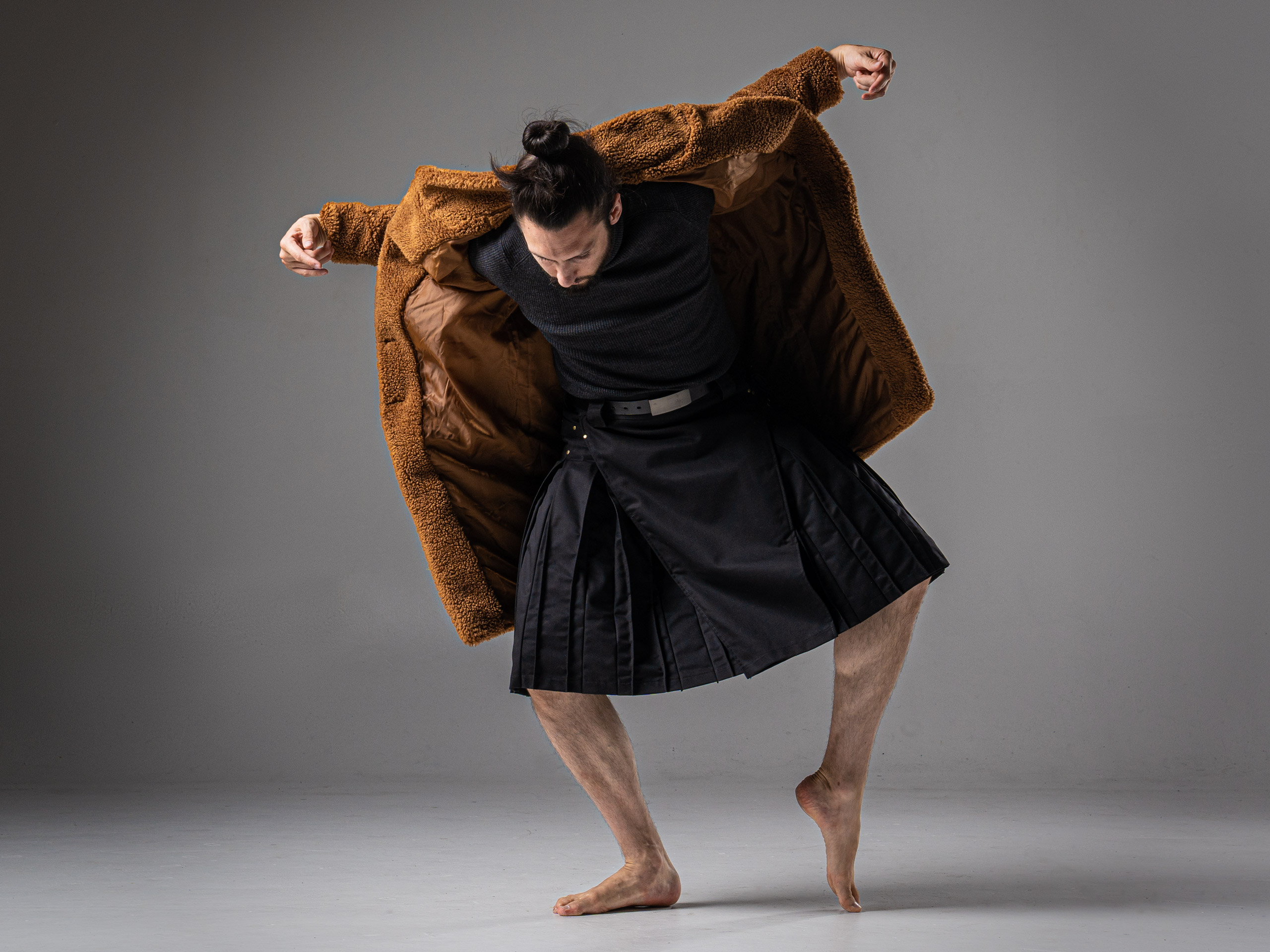 push/FOLD composer-choreographer Samuel Hobbs in a brown furry jacket and kilt holding a delicate and contorted pose.