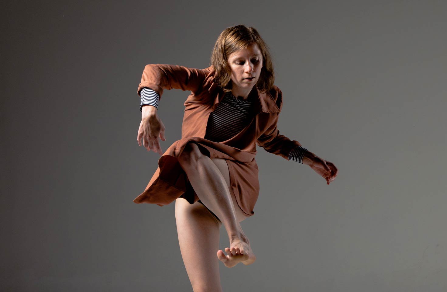 push/FOLD dancer Briley Jozwiak lifts up a gestural leg in an orange jacket at Cobalt Studios in Portland, Oregon | Photography: Jingzi Zhao