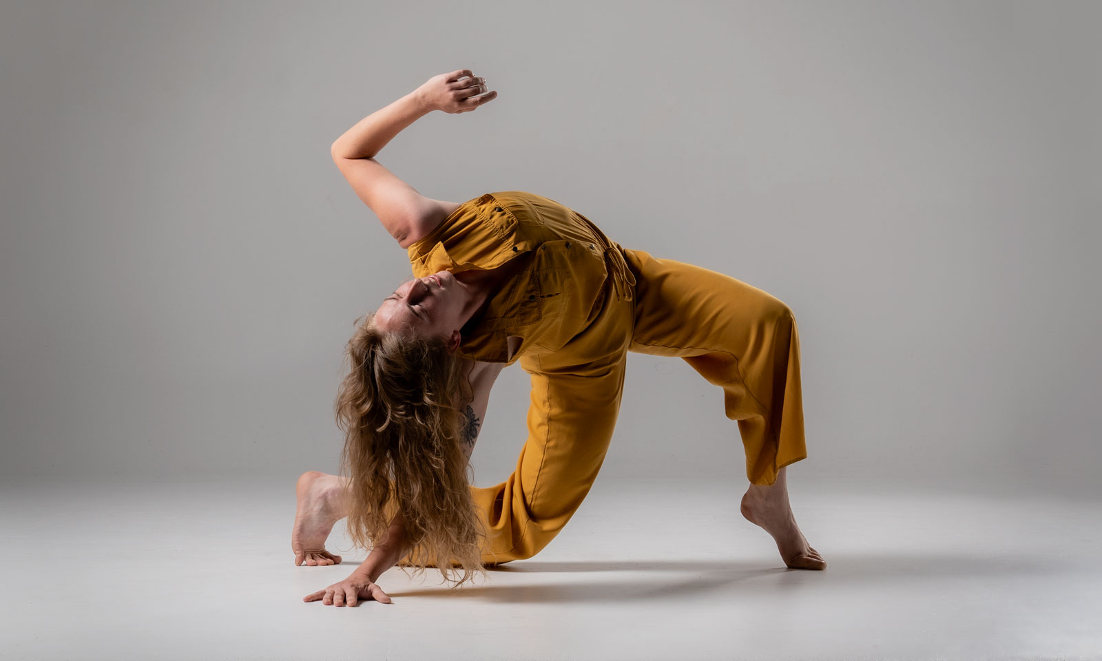 push/FOLD dancer Molly Rea wearing bright yellow overalls in full body twist on hands and feet at Cobalt Studios in Portland, Oregon | Photography: Samuel Hobbs